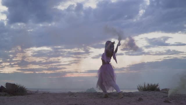 Sensual-young-woman-with-sparkling-makeup-in-a-pink-dress-dancing-with-smoke-bombs-on-the-bank-of-the-river.-The-dance-of-a-tender-sweet-girl-with-a-flower-hairstyle.-Slow-motion.