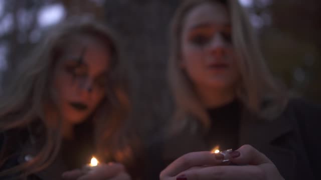 Porträt-von-zwei-Mädchen-mit-Halloween-Make-up-auf-Gesichtern-halten-kleine-Kerzen-in-den-Händen-in-die-Kamera-schauen.