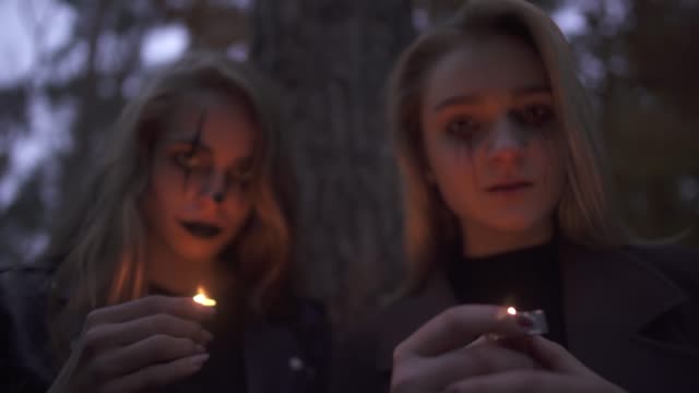 Portrait-of-two-girls-with-Halloween-makeup-on-faces-holding-small-candles-in-hands-looking-in-camera