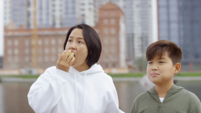 Asian-Mother-and-Son-Eating-Apples-on-City-Riverside