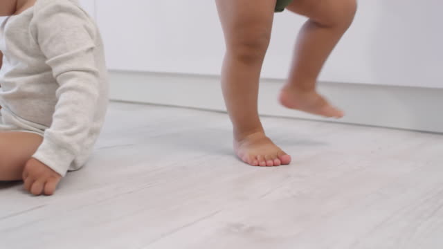 Nackte-Beine-des-Kleinkindes-lernen-zu-gehen-und-Geschwister-sitzen-auf-dem-Boden