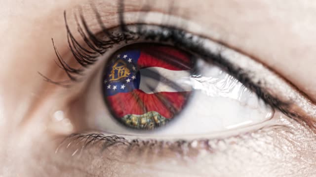 Mujer-ojo-verde-en-primer-plano-con-la-bandera-del-estado-de-Georgia-en-iris,-estados-unidos-de-América-con-movimiento-de-viento.-concepto-de-vídeo