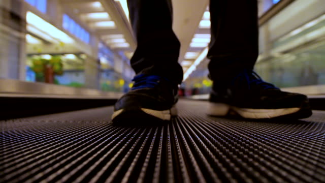 Closeup-front-view-on-man-legs-traveler-using-moving-flat-escalator-at-airport-terminal
