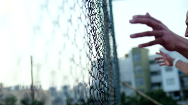 Angry-bald-man-beats-his-hands-on-a-grid-fence.-Aggressive-young-man