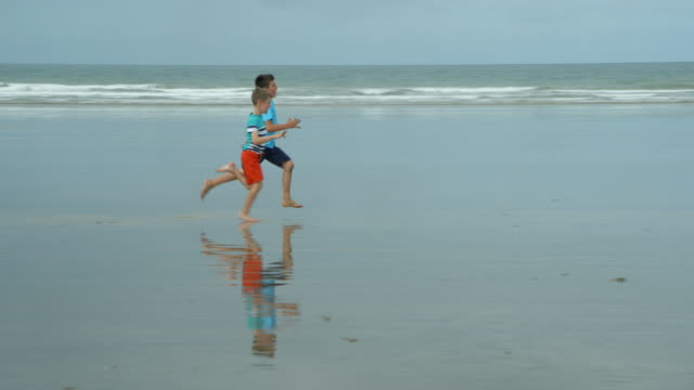 Two-boys-laughing-and-sprinting-along-a-beach-to-get-to-their-soccer-ball.