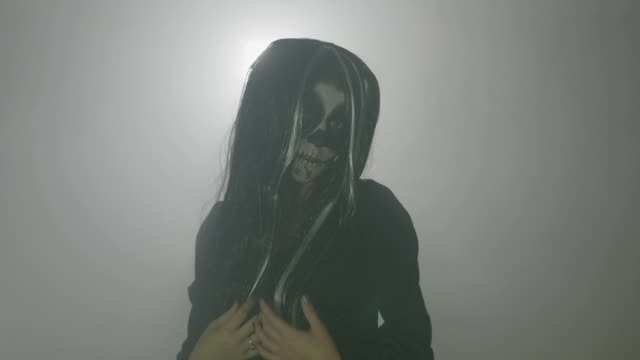 Creepy-evil-female-zombie-witch-wearing-a-wig-and-a-frightening-makeup-on-a-foggy-background-on-day-of-the-dead