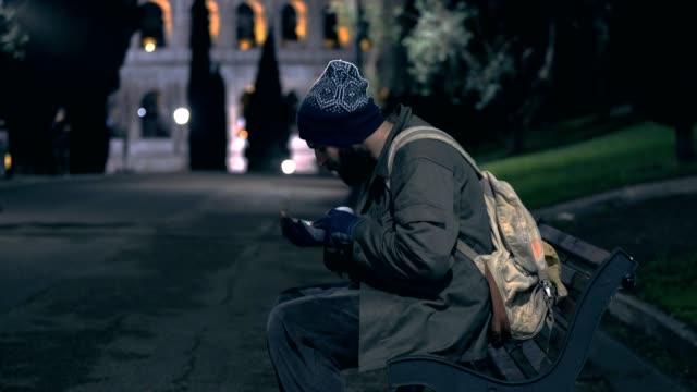 Lonely-homeless-sit-on-bench-at-night,-cheking-his-alms