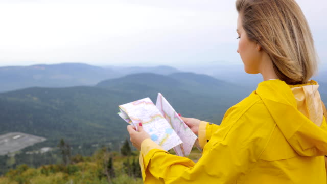 Junge-Frau-Im-gelben-Regenmantel-mit-einem-Rucksack-in-Bergen-Papierkarte-in-Händen-hält,-Wandern