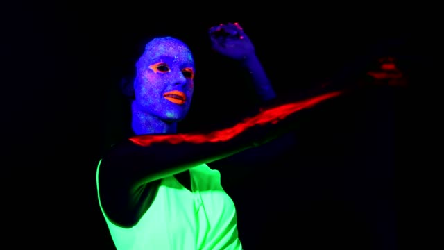 Woman-with-UV-face-paint,-glowing-clothing-dancing-fast-in-front-of-camera,-shoulder-face-shot.-Caucasian-woman.-.
