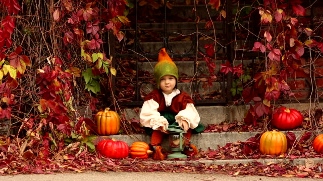 Entzückende-kleine-Mädchen-in-Gnome-Kostüm-Lächeln-beim-Sitzen-auf-der-Treppe-mit-Kürbissen-in-Halloween