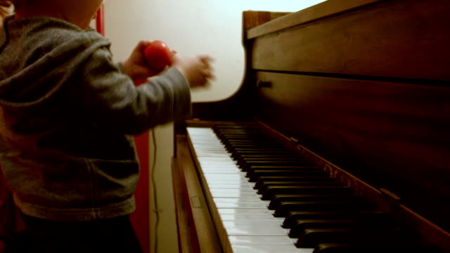 Caucásicos-niño-chico,-sentado-en-un-Piano-con-él-mamá,-juega-en-el-Piano-con-un-decorado-árbol-de-Navidad-detrás-de-ellos