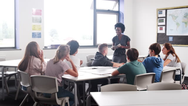 Weiblich-High-School-Lehrer-stehen-vom-Tisch-mit-Schülern-Unterricht