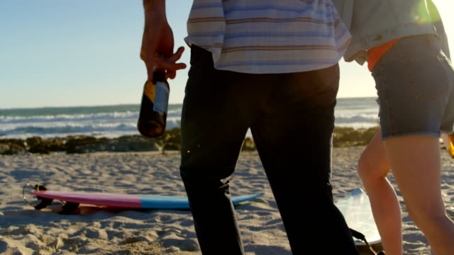 Rear-view-couple-holding-hands-with-beer-bottle-running-towards-the-beach-4k