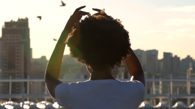 Junge-Afro-amerikanische-Frau-auf-Dach-sitzt-und-meditiert,-beobachtete-Stadtbild