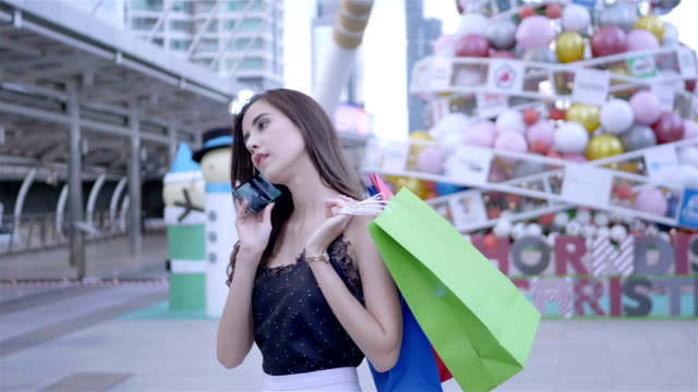 Schöne-Frau-mittels-Smartphone-und-Holding-Einkaufstaschen-glücklich-lächelnd-in-Stadt-Zentrum-Thailand.-Shopping,-Glück,-Technik-und-Mode-Konzept