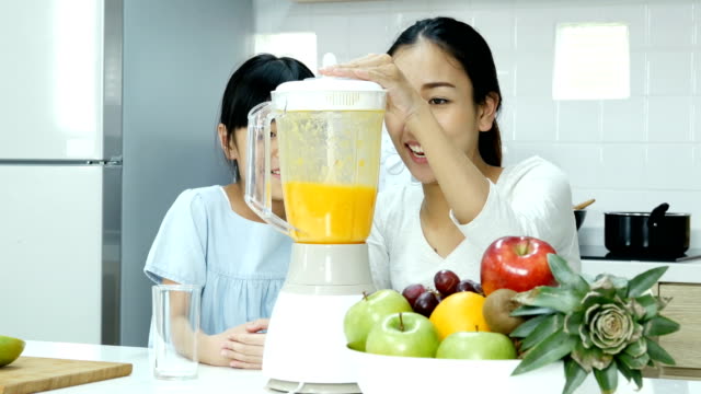 Mutter-und-mit-wenig-Saft-Mixer-in-der-Küche.-Sie-machen-Orangensaft-trinken.-Menschen-mit-Lebensstil-und-gesunde-Konzept.