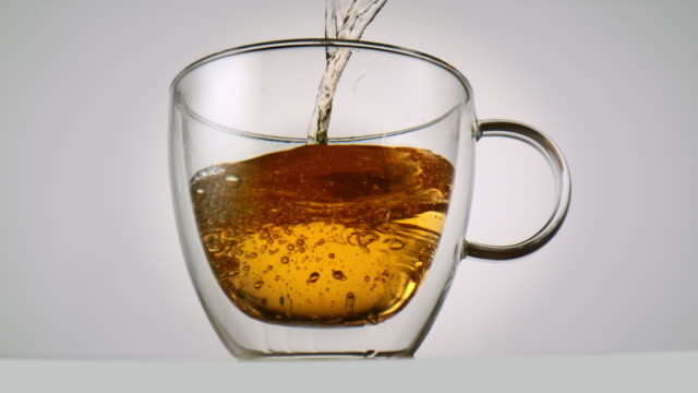 Pouring-tea-into-a-tea-glass-in-front-of-white-background-in-slowmotion
