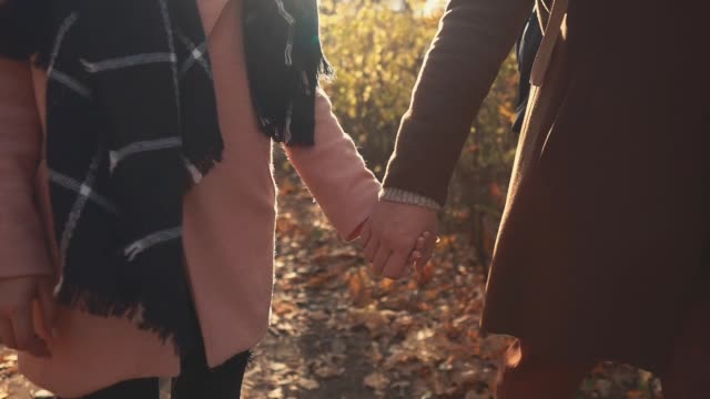 Romantic-close-up-view-of-joined-hands-of-man-and-woman-walking-in-fall-forest