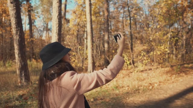 Young-blogger-girl-is-filming-herself-by-phone-on-walk-in-autumn-forest