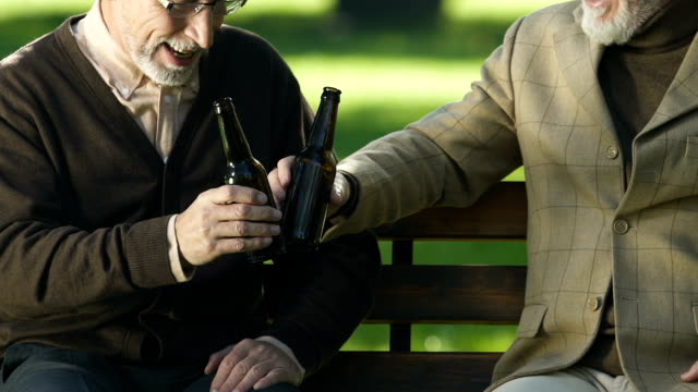 Senior-friends-drinking-light-beer-on-park-bench,-male-leisure,-celebration