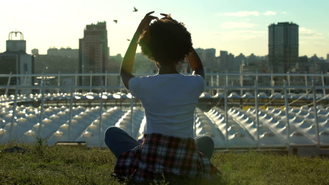 Relaxed-african-american-woman-sitting-in-lotus-pose,-meditating-at-sunset,-rest