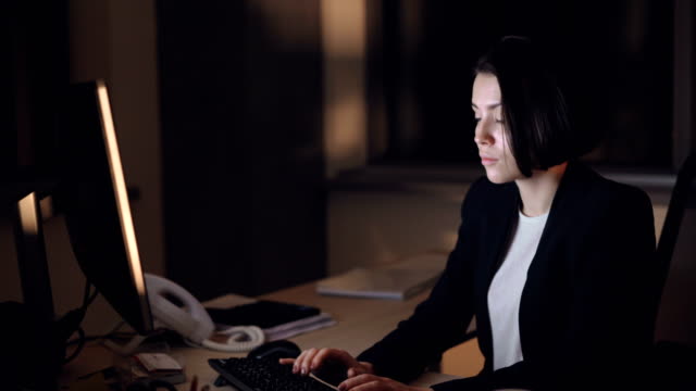 Businesswoman-in-formal-suit-is-working-on-computer-night-shift-sitting-at-desk-typing-and-looking-at-screen.-Busy-young-people,-overwork-and-career-concept.