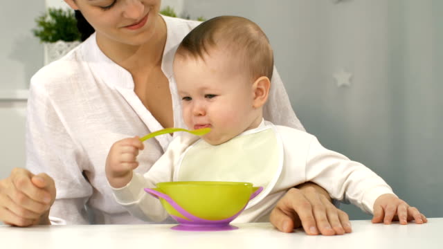 Baby-mit-Schüssel-und-Löffel-versuchen-zu-essen