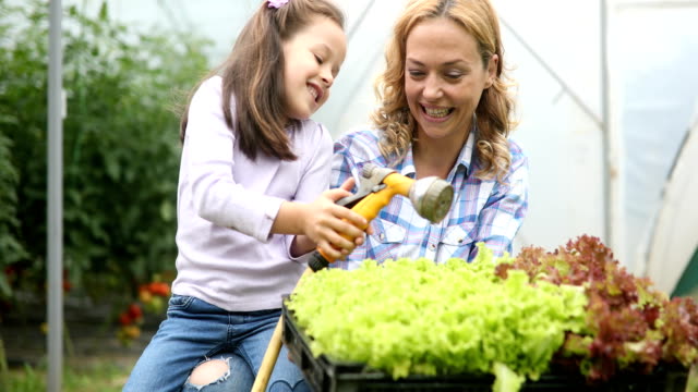 Farming,-gardening,-agriculture-and-people-concept.-Happy-mother-and-her-daughter-working-at-greenhouse