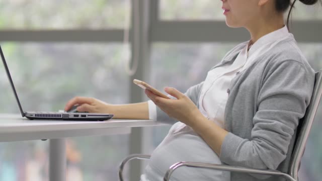 Chinesisch-schwangere-Bürofrau-arbeitet-mit-Laptop-und-Zelle