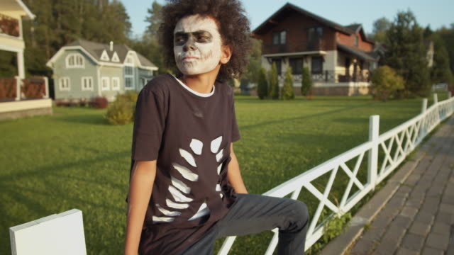 Junge-in-Halloween-Kostüm-sitzen-auf-Zaun