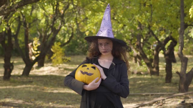Bonita-pelirroja-caucásica-vestida-con-traje-de-bruja-de-Halloween-de-pie-en-el-parque-de-otoño.