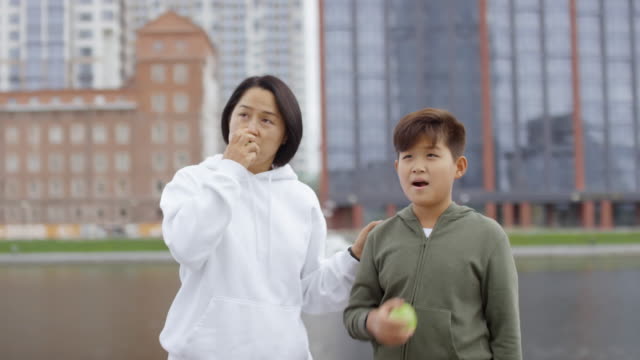 Asian-Mother-and-Son-Eating-Apples-and-Talking-on-Urban-Riverside