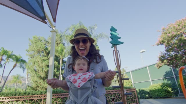 POV-sliding-on-slide-at-playground-to-meet-mother-with-baby-on-carrier