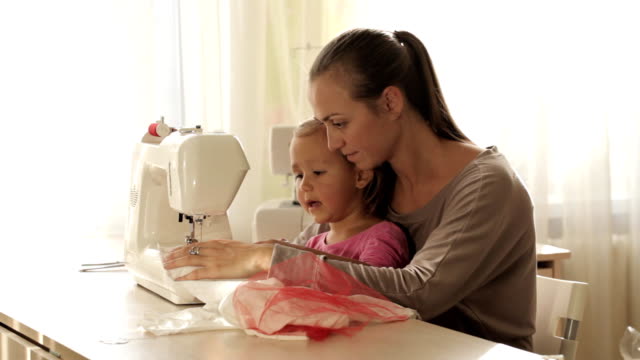 Joven-atractiva-madre-trabajando-en-la-máquina-de-coser-con-su-hija-poco-Linda