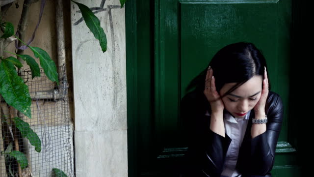 Traurige-und-verzweifelte-junge-Asiatin,-die-auf-einen-Schritt-auf-der-Straße-sitzen