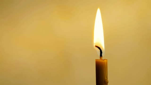 Close-up-of-a-wax-candle-burns-on-a-yellow-background.-4K.