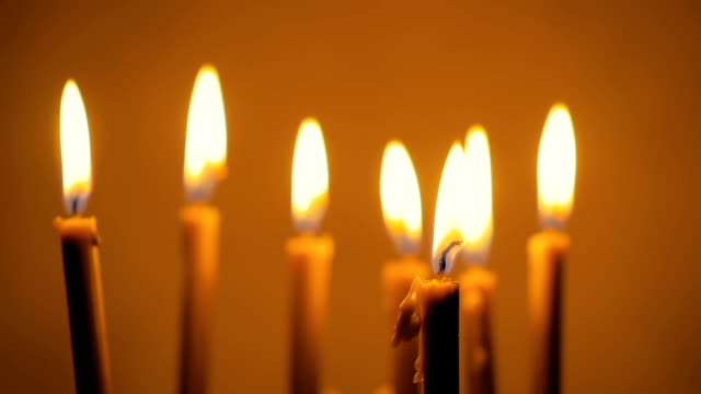 Close-up-of-a-lot-of-beautiful-wax-candles-burning.-Yellow-background.