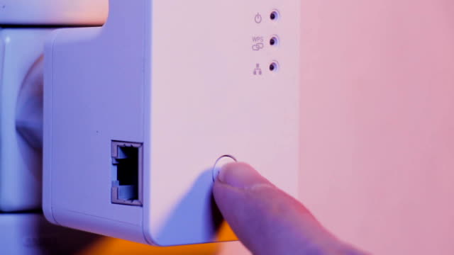 Man-press-with-his-finger-on-WPS-button-on-WiFi-repeater-which-is-in-electrical-socket-on-the-wall