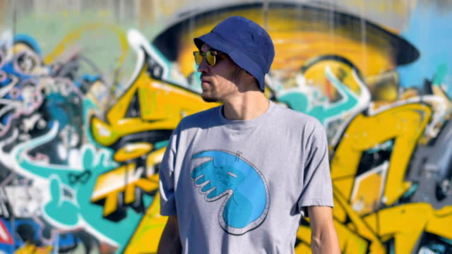Portrait-of-adult-man-is-standing-with-a-graffiti-painting-in-the-background-and-glancing-around