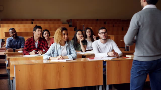 Multiracial-students-are-raising-hands-and-answering-teacher's-questions,-guy-in-glasses-gives-correct-answer-and-is-boasting-about-it.-Classmates-and-college-concept.
