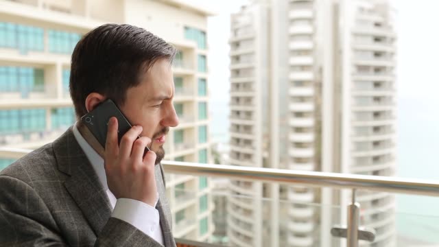 Hombre-de-negocios-enojado-hablando-por-teléfono,-de-pie-en-el-balcón.-Fondo-de-la-gran-ciudad