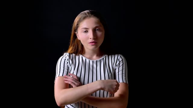 Furious-young-woman-standing-with-crossed-hands-and-looking-at-camera-with-angry-and-concerned-expression,-black-background