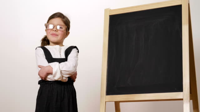 Ein-fröhliches-Mädchen-gekleidet-wie-ein-Lehrer-vor-einer-kleinen-Tafel-hält-den-verschränkten-Armen-und-lächelt.
