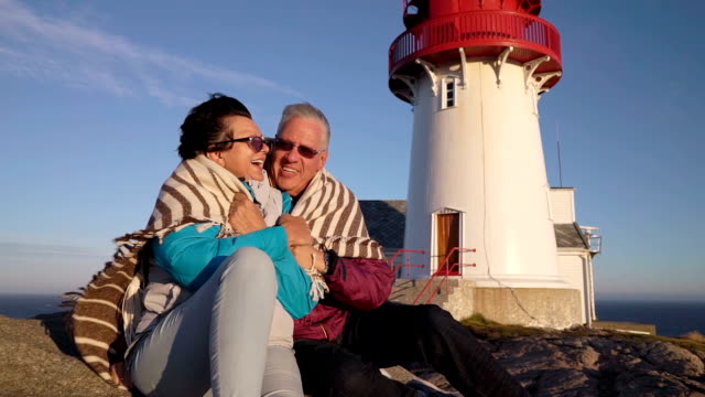 A-Mature-couple-admires-the-sunset-on-the-sea-coast-with-an-old-lighthouse.