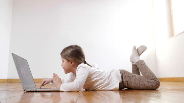 Ein-kleines-Mädchen-auf-dem-Boden-liegend-den-Computer-benutzt-und-schaut-in-die-Kamera-und-das-Lächeln.