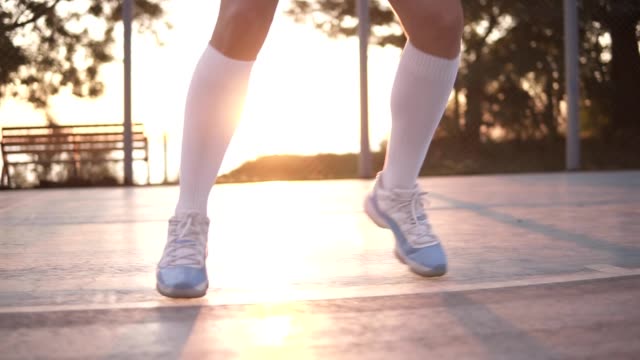 Close-up-of-female-basketball-player-legs-in-white-golf-socks-doing-dribbling-exersice-very-quickly,-run-backwards,-training-outdoors-on-the-local-court.-Sun-shines-on-the-background