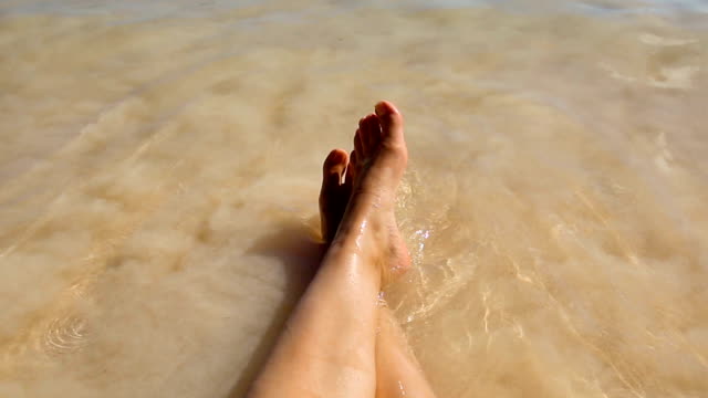 The-coastal-wave-of-the-warm-calm-sea-washes-two-feet-of-a-woman-resting-on-the-beach.