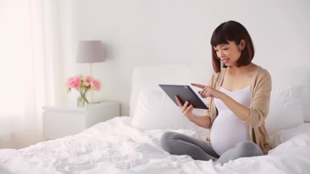 glücklich-schwanger-Asiatin-mit-Tablet-pc-zu-Hause