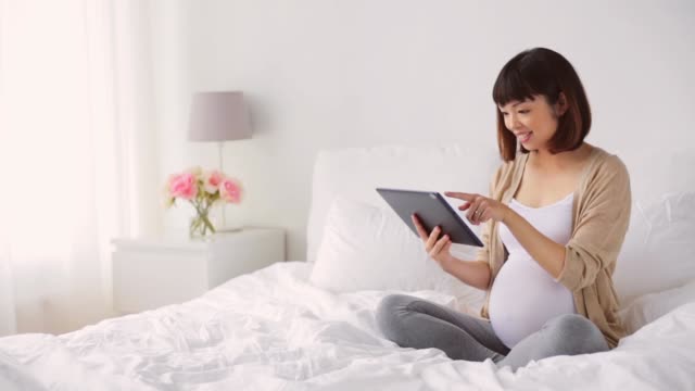feliz-embarazada-mujer-asiática-con-tablet-pc-en-el-hogar