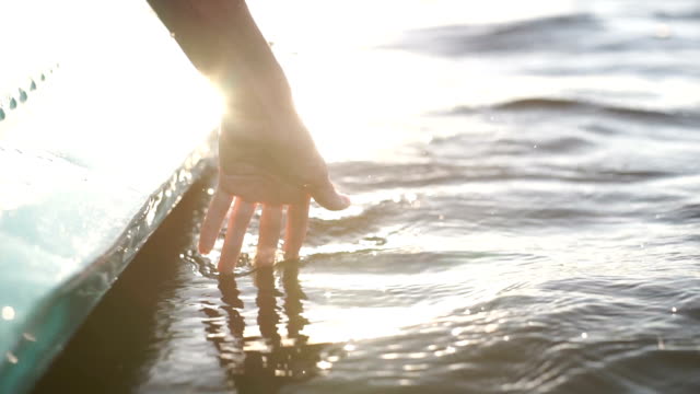At-sunset,-close-up-the-hand-of-a-girl-moving-through-the-water